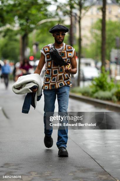 Guest wears a black felt beret, black sunglasses, a black shiny leather fanny pack bag, a silver chain necklace, a white with brown and dark green...