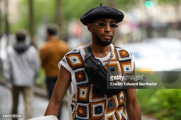 Guest wears a black felt beret, black sunglasses, a black shiny leather fanny pack bag, a silver chain necklace, a white with brown and dark green...