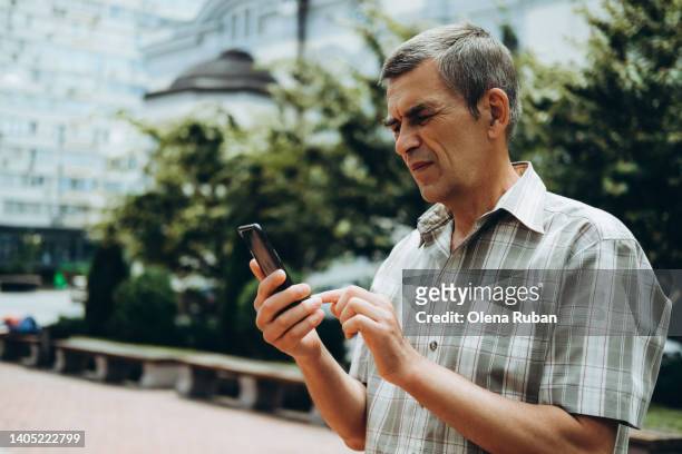 man typing on mobile phone against trees and buildings. - entrecerrar los ojos fotografías e imágenes de stock