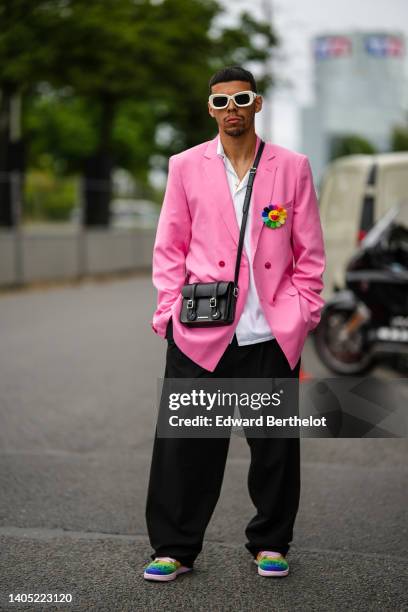 Guest wears white sunglasses, a white shirt, a pink oversized blazer jacket with embroidered multicolored flower pins, a black shiny leather...