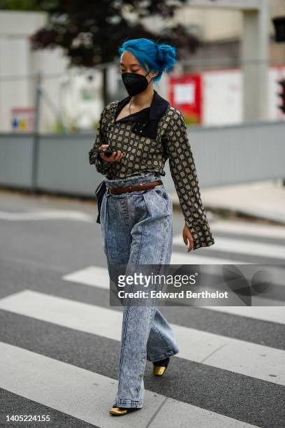 Guest wears silver earrings, a gold and black checkered print pattern open high neck / long sleeves shirt, a black shiny leather shoulder bag from...