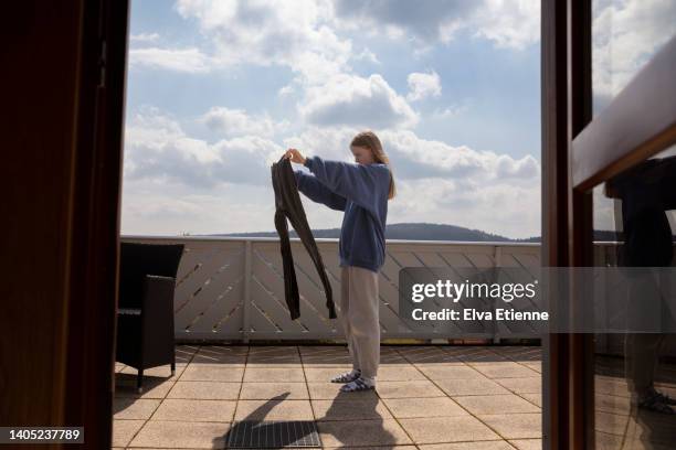 teenage girl checking laundry on an outdoor balcony with a backdrop of distant hilltop forests and blue sky with fluffy clouds in springtime. - pantaloni di tuta foto e immagini stock
