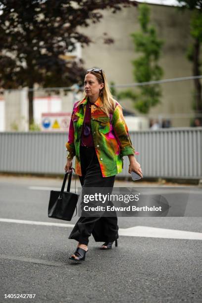 Guest wears black sunglasses, a gold chain pendant necklace, a burgundy t-shirt, a purple suede necklace bag, a green / yellow / orange / black tie...