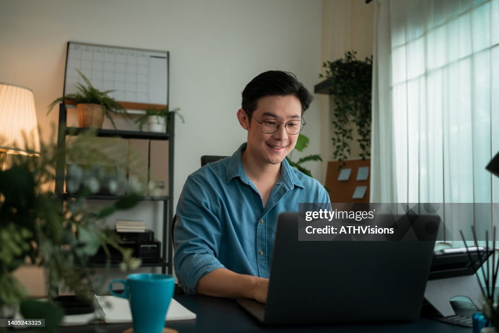 Homme heureux et souriant Tapant un e-mail à son client. Il a une réunion virtuelle en ligne sur ordinateur portable à la maison.