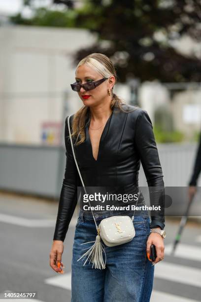 Guest wears black sunglasses, gold earrings, a black V-neck shiny leather jacket, pale gray with embroidered gold star crossbody bag from YSL / Saint...