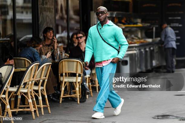 Guest wears black sunglasses, a red and white tie and dye print pattern shirt, a green blue fluffy polo pullover, blue ribbed large pants, a silver...