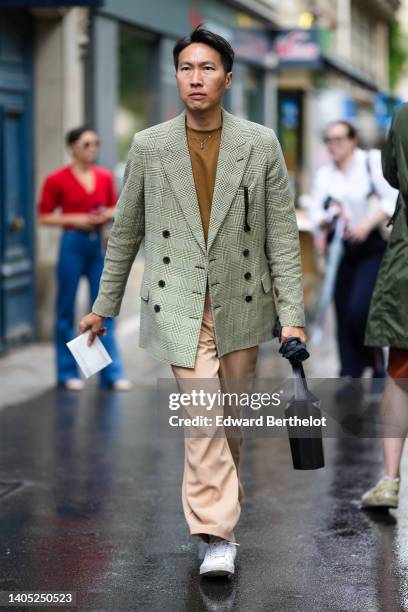 Guest wears black sunglasses, a gray checkered print pattern blazer jacket, beige suit pants, black shiny leather handbag, white socks, white shiny...