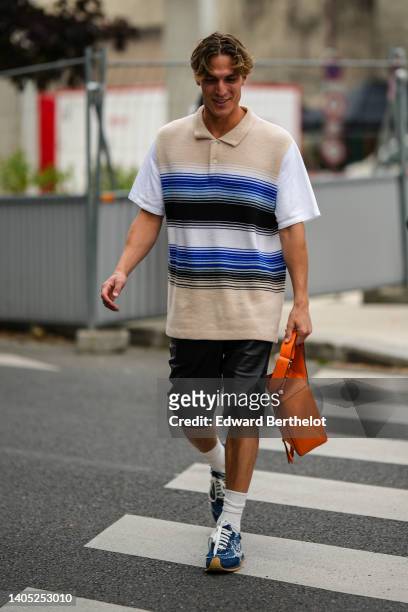 Guest wears a beige with black and blue striped print pattern with white short sleeves oversized polo shirt, black shiny leather shorts, an orange...