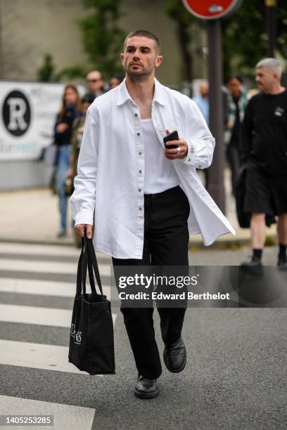 Guest wears a white t-shirt, a white oversized open shirt, black suit pants, a black cotton handbag, black shiny leather ankle boots , outside the...