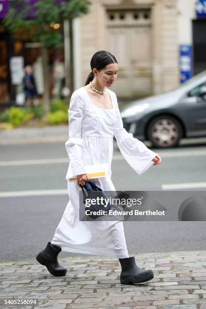 Guest wears a white pearls necklace, a white square-neck / puffy long sleeves / long ruffled dress, a black plastic ankle boots from Bottega Veneta,...