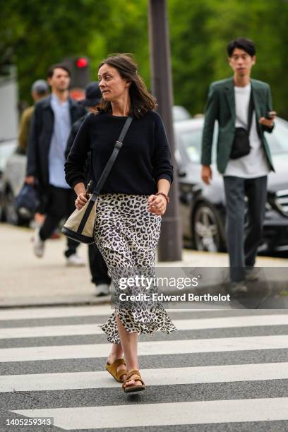 Guest wears a black wool pullover, a black shiny leather with beige fabric crossbody bag, a white latte with black leopard print pattern midi skirt,...