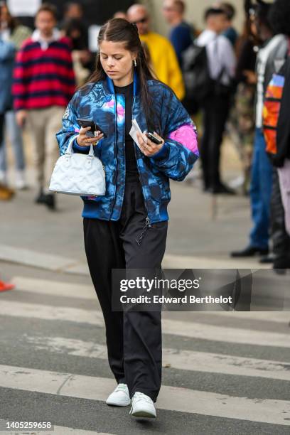 Guest wears white pearls earrings, a black t-shirt, black large pants, a navy blue and pink tie and dye print pattern bomber coat, a pale blue...