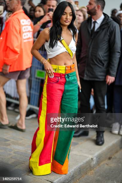Amina Muaddi wears a white V-neck / rolled-up waist / cropped tank-top, a yellow shiny leather Puzzle crossbody bag from Loewe, green / red / yellow...