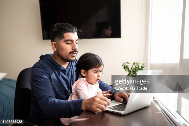 father using the laptop with daughter on his lap at home - busy toddlers stock pictures, royalty-free photos & images