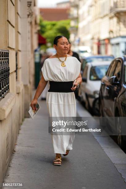 Guest wears a gold large chain pendant necklace, a white short sleeves / large belt / long dress, gold bracelets, a silver watch, gold rings, gold...