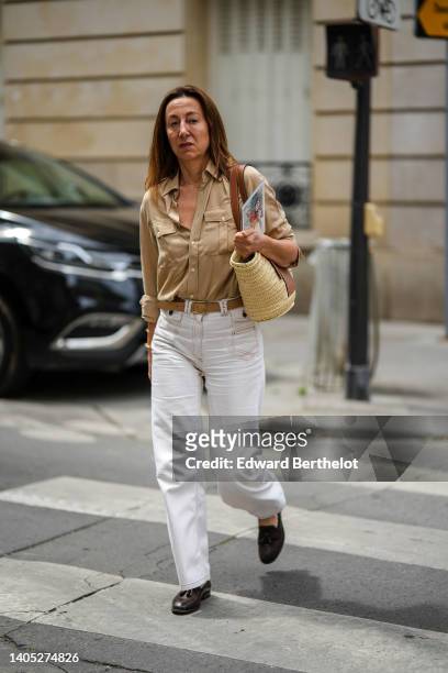 Guest wears a beige cargo pants, a brown leather belt, white denim flared pants, a beige wickers shoulder bag from Loewe, black shiny leather...