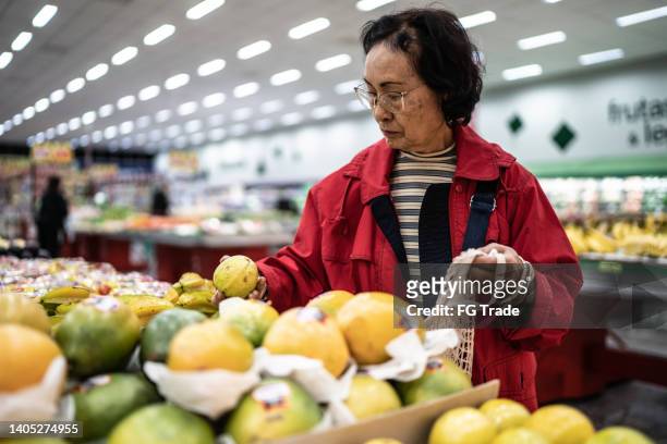 portrait of a senior woman choosing guava in a supermarket - guava fruit stock pictures, royalty-free photos & images