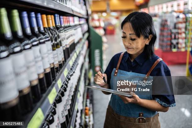 reife frau, die mit einem digitalen tablet in einem supermarkt arbeitet - tablet alcohol stock-fotos und bilder