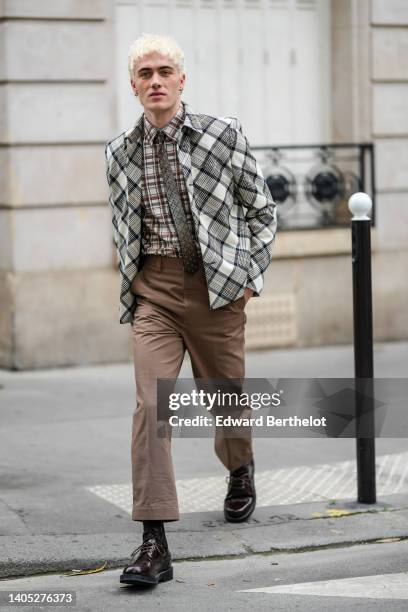 Guest wears silver earrings, a brown and beige checkered print pattern shirt, a gray and white checkered print pattern blazer jacket, brown suit...