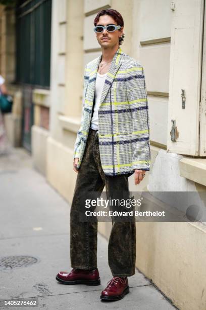 Guest wears blue sunglasses, silver earrings, a white with black and yellow checkered print pattern oversized blazer jacket, black and brown tie and...