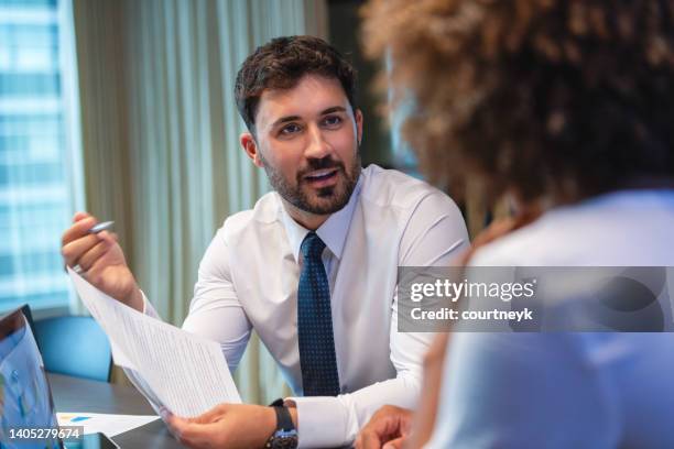 business man talking to a business woman while holding a document. he is happy and smiling. he is wearing a tie. - lawyer stockfoto's en -beelden