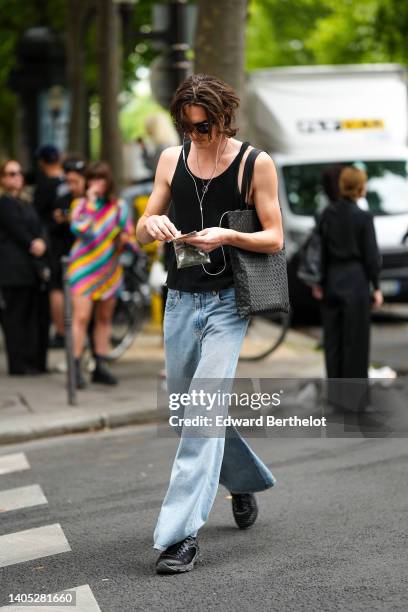 Guest wears black sunglasses from Ray Ban, a black tank-top, a black large shoulder bag, blue faded denim flared pants, black embossed striped...