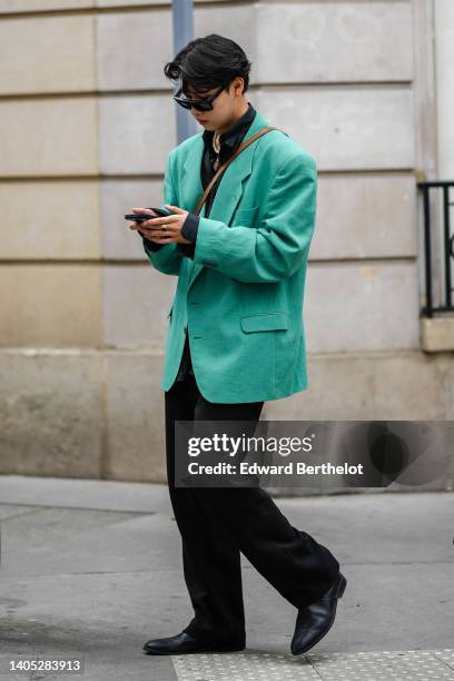 Guest wears sunglasses, a black shirt, a white pearls necklace, a green oversized blazer jacket, black suit pants, black shiny leather ankle boots,...