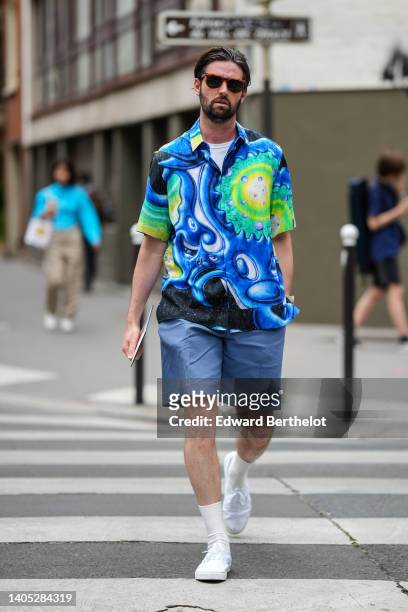 Guest wears sunglasses, a white t-shirt, a royal blue / yellow / neon green / white print pattern short sleeves shirt from Dior, blue gray suit...