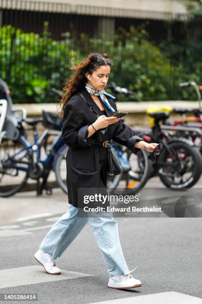 Guest wears a blue / beige / gold print pattern silk scarf, a black long blazer jacket, a black shiny leather GG buckle belt from Gucci, a black...