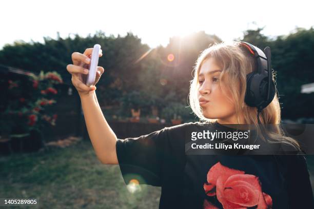 happy teen girl in headphones takes a selfie on the phone or talks on the phone. - girl selfie fotografías e imágenes de stock