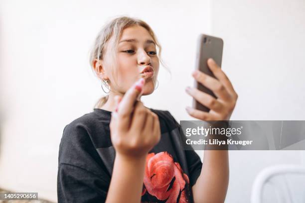 teenage girl paints her lips using a phone instead of a mirror. - child mobile phone stockfoto's en -beelden
