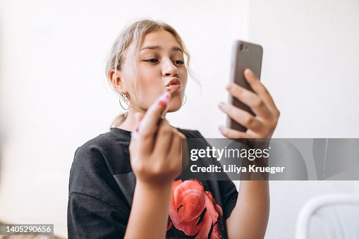 Teenage girl paints her lips using a phone instead of a mirror. Teenage girl paints her lips using a phone instead of a mirror.