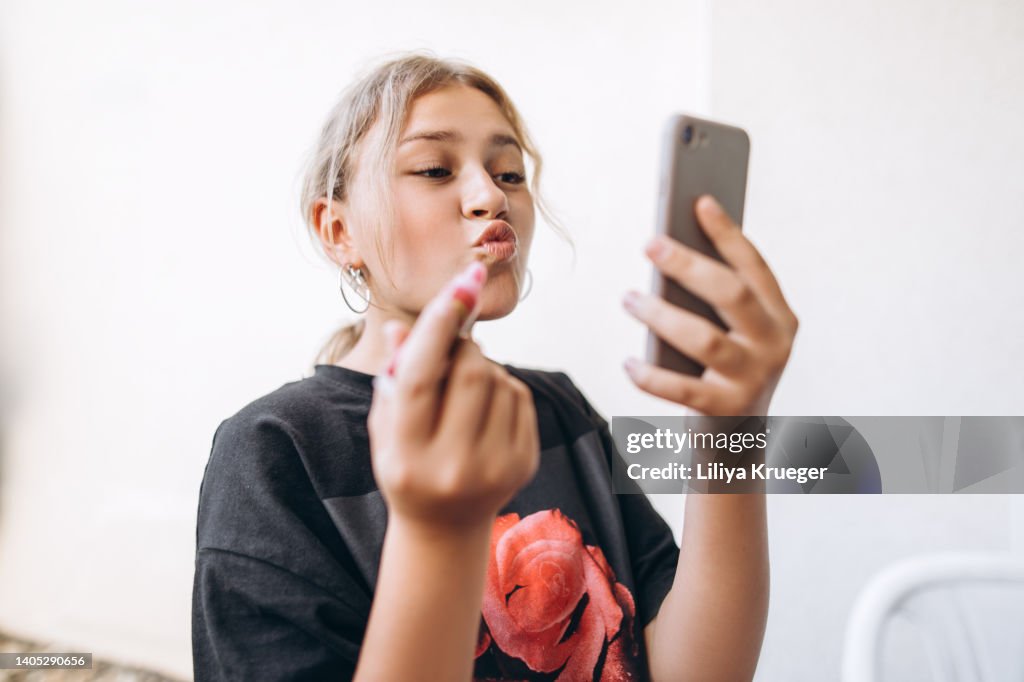 Teenage girl paints her lips using a phone instead of a mirror.