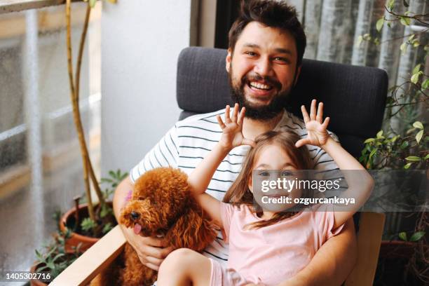 happy father and daughter having fun with their toy poodle on the sofa - smiling brown dog stock pictures, royalty-free photos & images