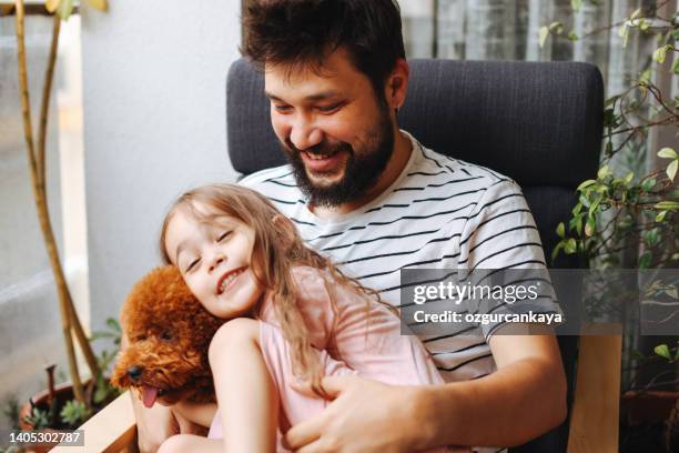 happy father and daughter having fun with their toy poodle on the sofa - smiling brown dog stock pictures, royalty-free photos & images