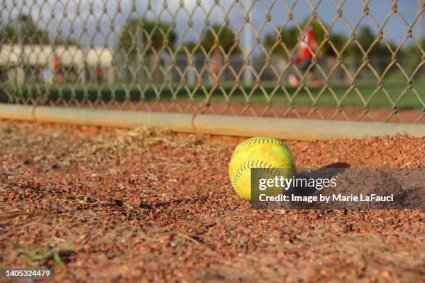 close-up of a yellow softball on gravel near fence - yankees home run stock pictures, royalty-free photos & images