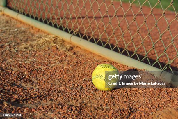 close-up of a yellow softball on gravel near chainlink fence - yankees home run stock pictures, royalty-free photos & images