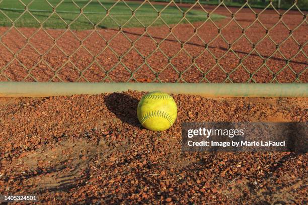 close-up of a yellow softball on gravel near chainlink fence - softball stockfoto's en -beelden