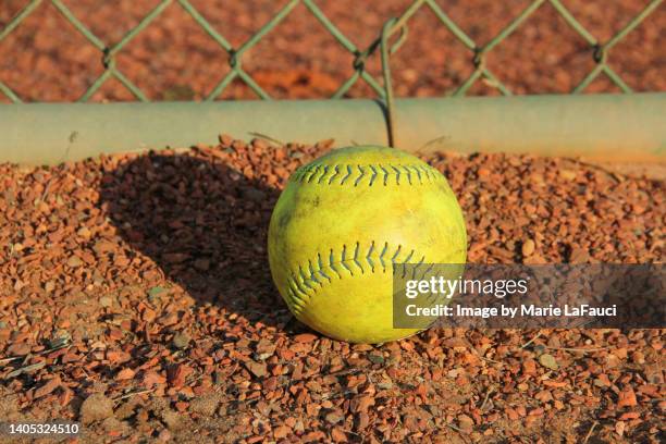 close-up of a yellow softball on gravel near chainlink fence - yankees home run stock pictures, royalty-free photos & images