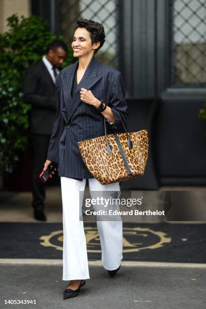 Farida Khelfa wears a black V-neck blouse, a black with white small striped print pattern oversized blazer jacket, white denim wide legs pants, a...