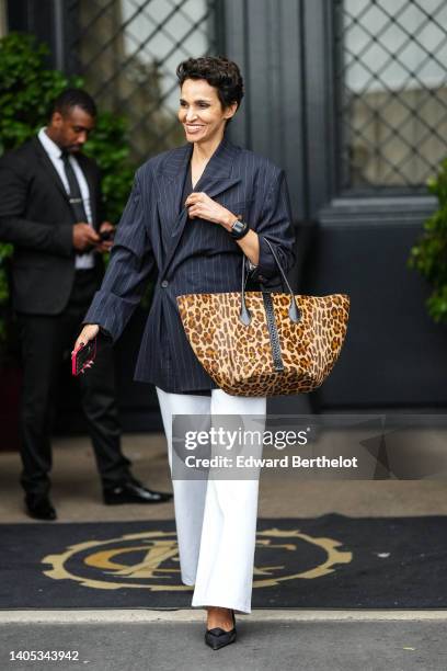 Farida Khelfa wears a black V-neck blouse, a black with white small striped print pattern oversized blazer jacket, white denim wide legs pants, a...