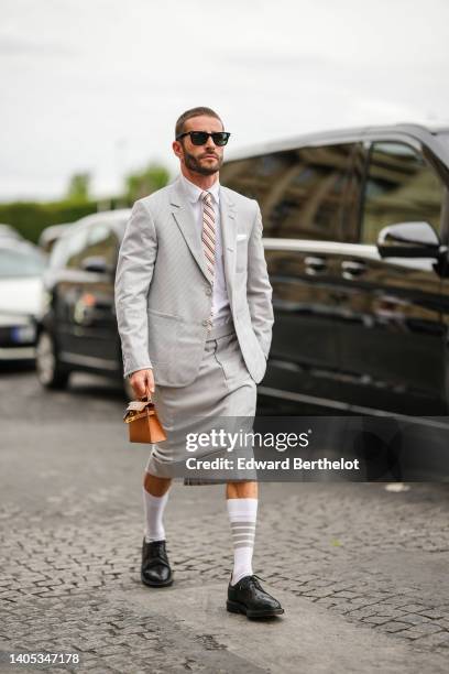 Pelayo Diaz wears black Ray Ban sunglasses, a white shirt, a white latte with red and navy blue striped print pattern tie, gray checkered print...