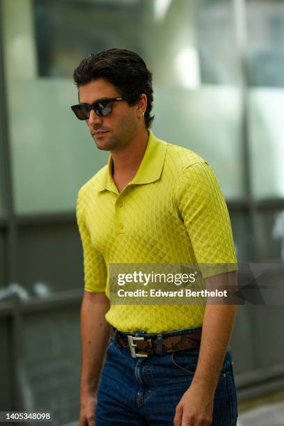 Marc Forne wears black sunglasses, a yellow embossed triangular pattern short sleeves / polo shirt, a brown and black shiny leather snake print...