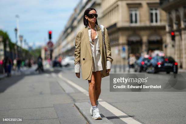 Alexandra Guerain wears black sunglasses from Chanel, silver and gold earrings from Louis Vuitton, a white latte linen shirt, a beige oversized...