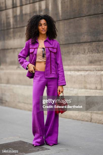 Guest wears a beige shoulder-bag / cropped top, black sunglasses, a neon purple with embroidered burgundy borders denim jacket, matching purple denim...