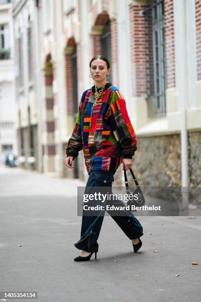 Guest wears gold earrings, a long / large gold chain necklace, a multicolored print pattern high neck /oversized sweater, navy blue cargo pants,...