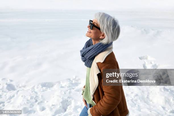 adult woman in sunglasses stands on a background of snow - mature woman winter stock-fotos und bilder