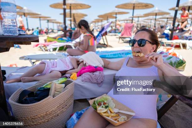 woman eating souvlaki on the beach, while taking care of her toddler daughter while she sleeping - souvlaki stock pictures, royalty-free photos & images