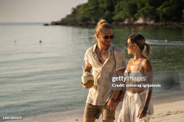 ビーチを歩くのんきな若いカップル - 2 coconut drinks ストックフォトと画像