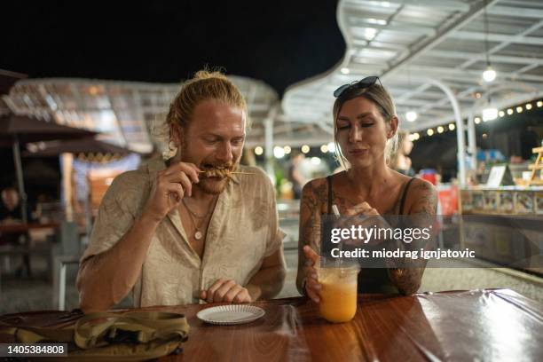 caucasian couple eating and drinking at the night market - street food market stock pictures, royalty-free photos & images
